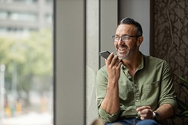 Man in green shirt sitting at window talking into cell phone