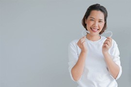 Smiling woman in white shirt holding her clear aligners