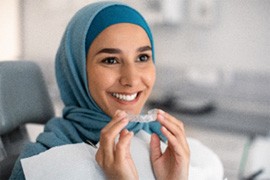 Smiling woman in dental office holding Invisalign aligner