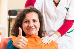 Smiling woman in dental chair giving thumbs up